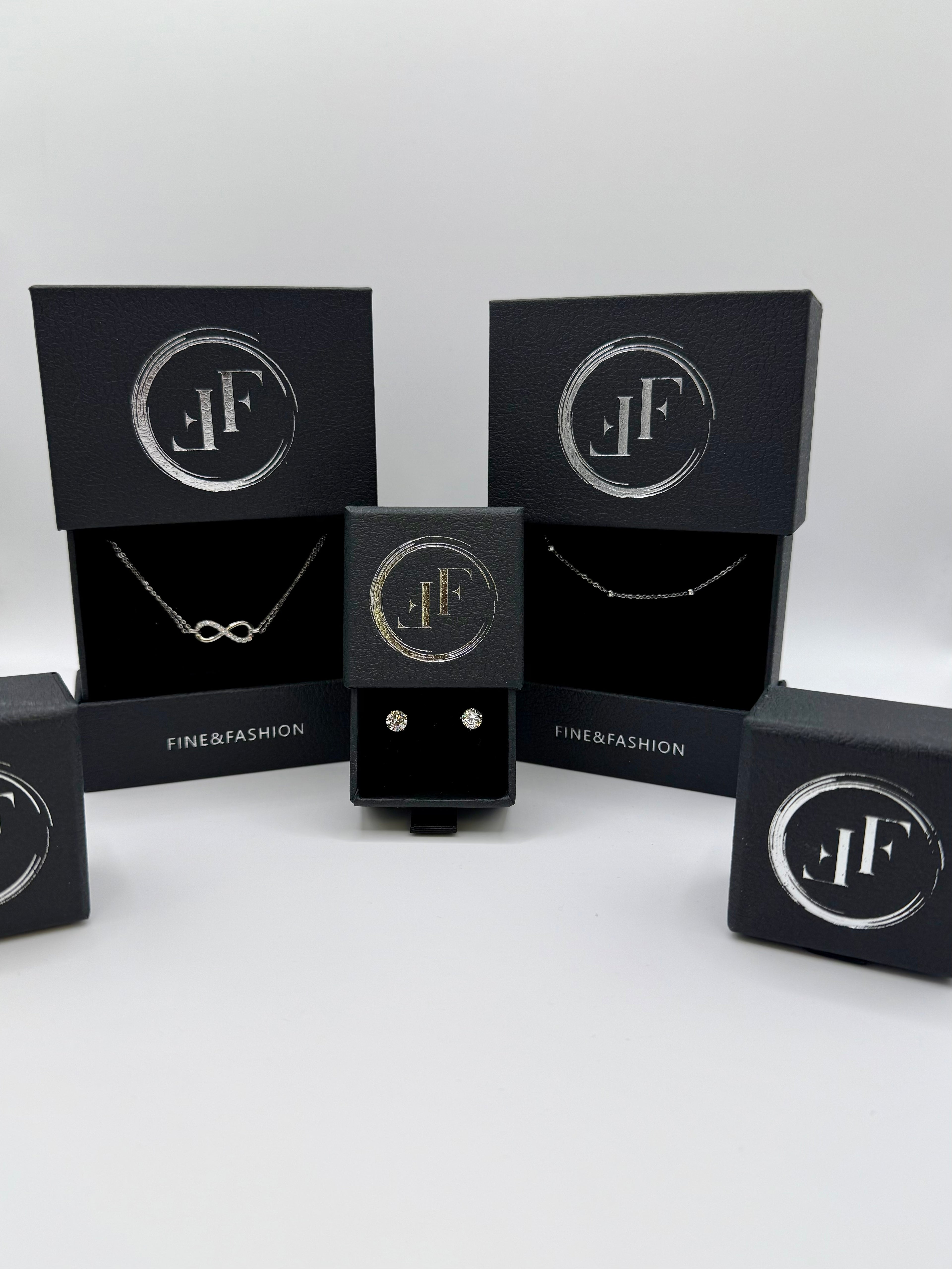 Jewelry set with necklaces and earrings in black boxes featuring a logo on a white background